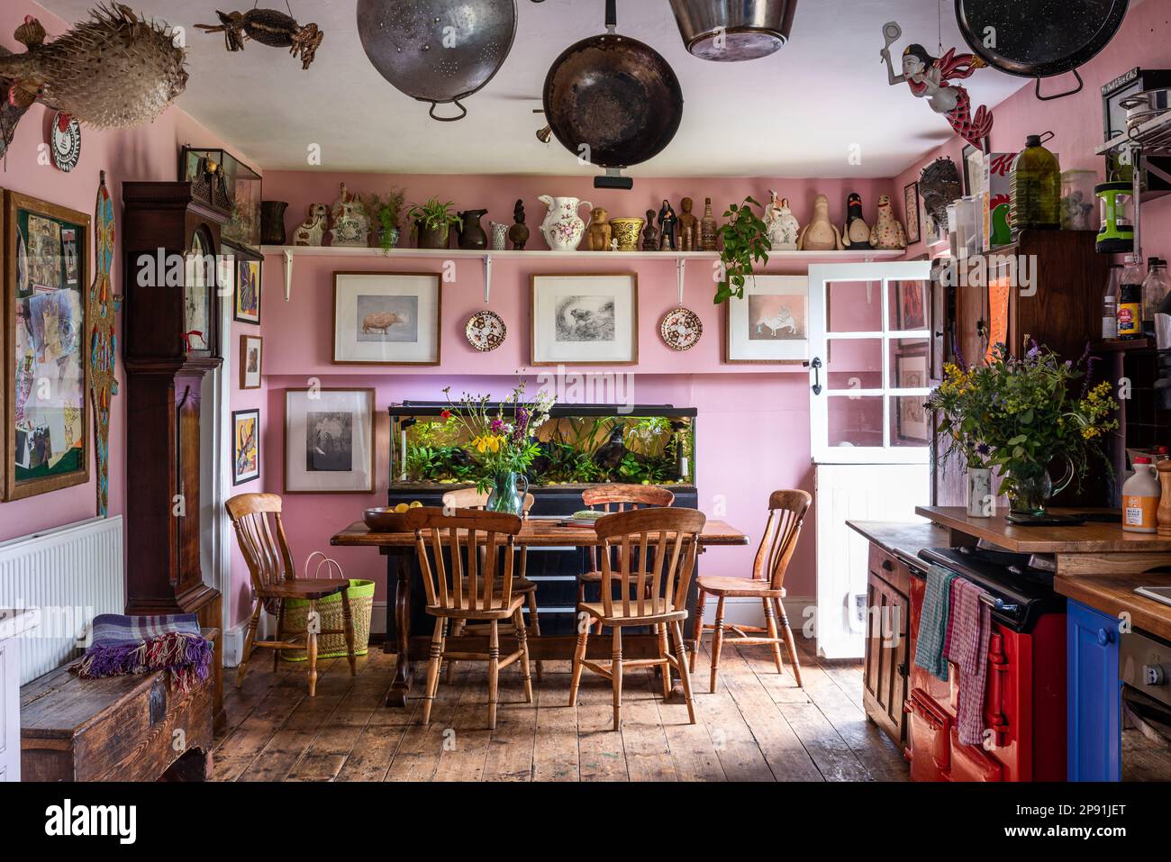 Töpfe, Pfannen und gerahmte Kunstwerke mit Original-Aga in rosafarbener Küche des Bauernhauses von Tudor aus dem 16. Jahrhundert, Suffolk, Großbritannien. Stockfoto