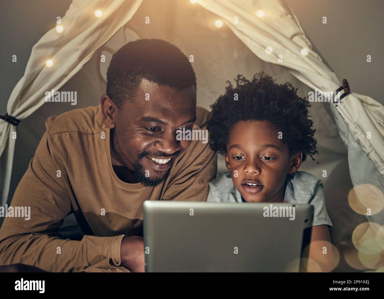 Schwarze Familie, Tablet und Vater mit einem Kind im Zelt, das sich nachts einen Film, ein Video ansieht und zu Hause Spaß hat. Technologie, Bokeh und Lächeln des glücklichen Vaters Stockfoto