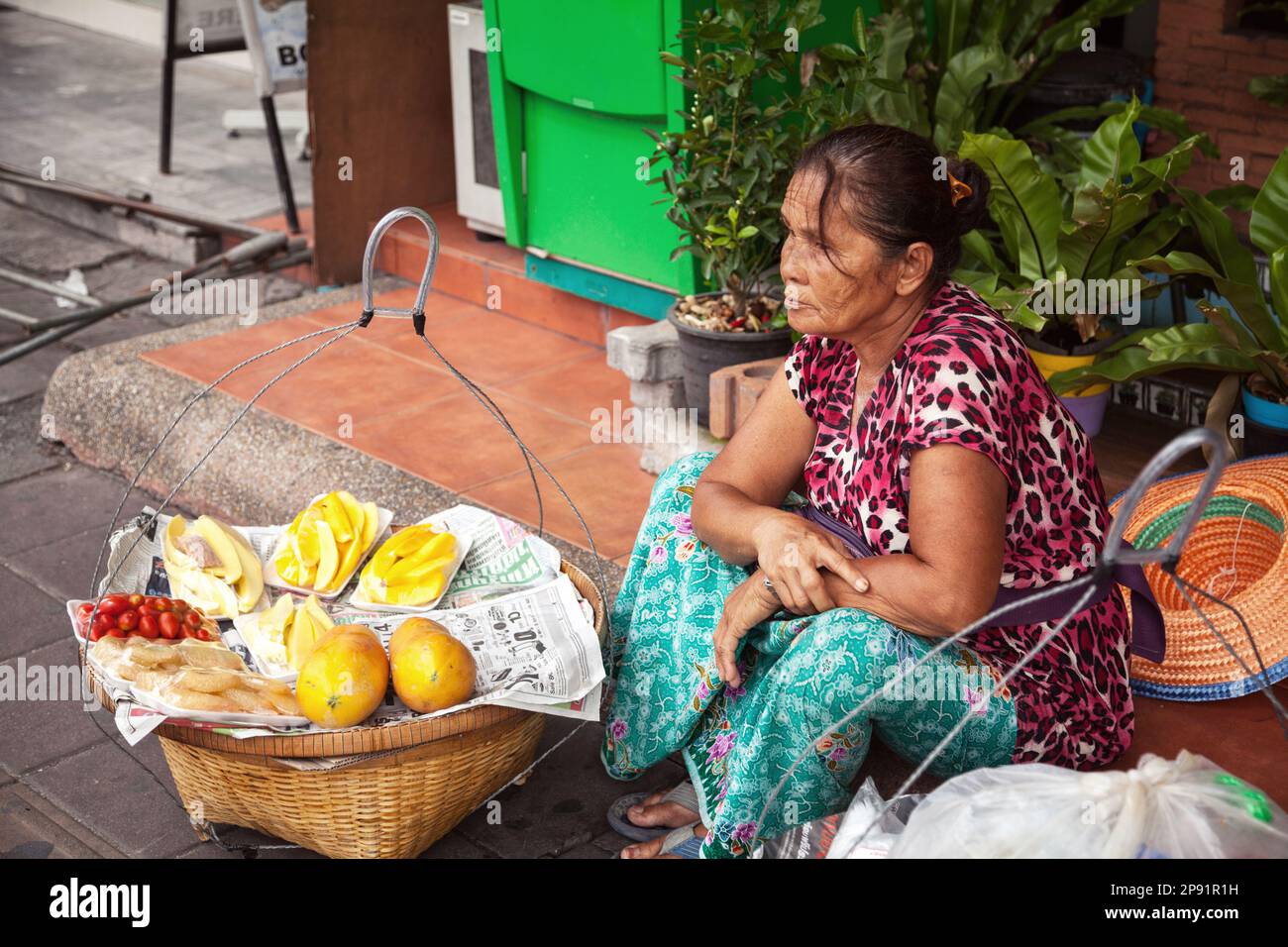 Pattaya, Thailand - 28. März 2016: Thailändischer Straßenverkäufer, der Obst aus Körben verkauft. Lebensmittelverkäufer sitzt auf dem Bürgersteig Stockfoto