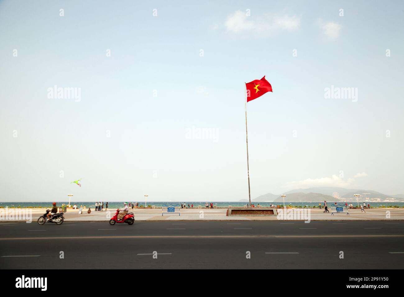 Stadtbild der Stadt Nha Trang mit einem roten Vietnamesische Flag. Motorräder fahren entlang der Beach Road. Text auf eine Flagge Sockel: Platz 2-4 Stockfoto