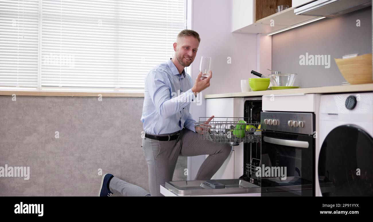 Junger Mann, Der Trinkglas Aus Der Spülmaschine In Der Küche Nimmt Stockfoto