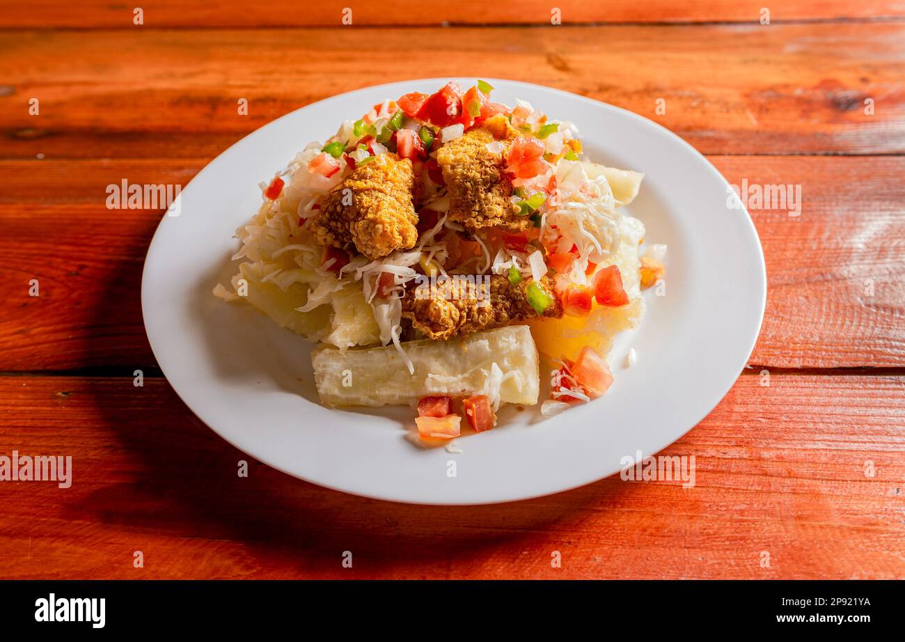 Traditionelles Chicharron-Gericht mit Kassava und Tomatensalat. Lateinische Küche Chicharron con Yuca serviert auf Holztisch. Nicaraguanisches Gericht mit Chicharron Stockfoto