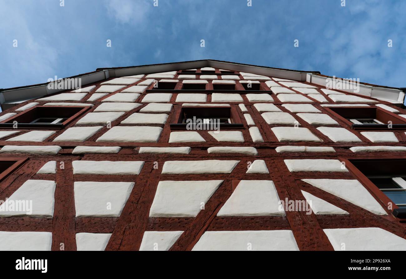 Aus der Perspektive des Frosches sehen Sie ein Fachwerkhaus mit weißen Wänden und roten Holzbalken unter einem blauen Himmel im malerischen Dorf Stockfoto