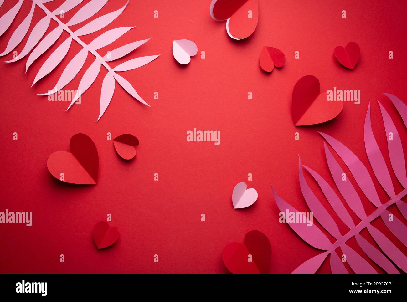 Flach liegender romantischer Valentinstag Hintergrund, Papierkunst Dekoration. Papierherzen und tropische exotische Blätter auf festlichem roten Hintergrund. Valentinstag Stockfoto