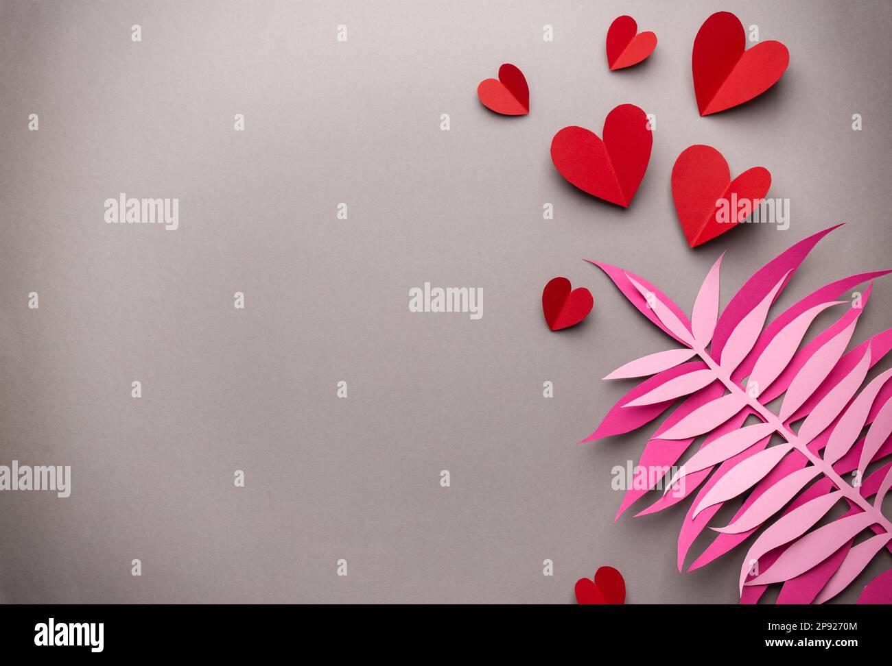 Flach liegender romantischer Valentinstag Hintergrund, Papierkunst Dekoration. Papierherzen und tropische exotische Blätter auf neutralem grauen Hintergrund. Valentinstag Stockfoto