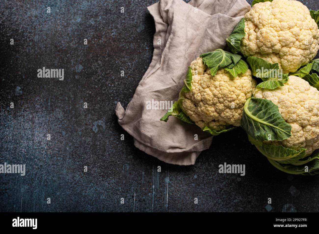 Frischer, ganzer organischer, weißer Blumenkohl auf dunklem Stein-Hintergrundtisch, fertig zum Kochen, Draufsicht mit Kopierbereich. Vegetarisches Essen, sauber Stockfoto