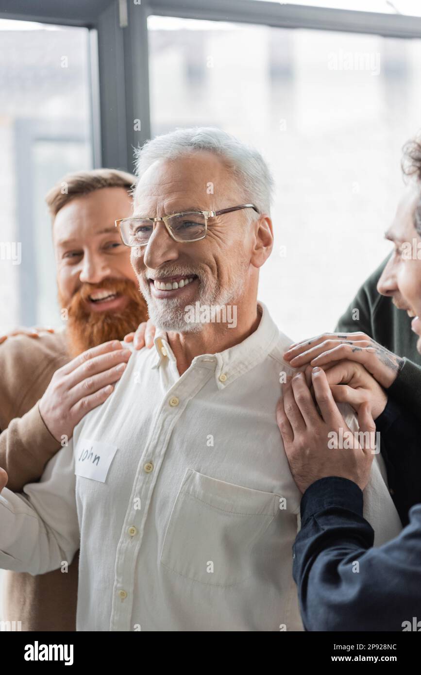 Positive Menschen umarmen Männer mittleren Alters mit Alkoholsucht während der Gruppentherapie im Reha-Zentrum,Stock Image Stockfoto