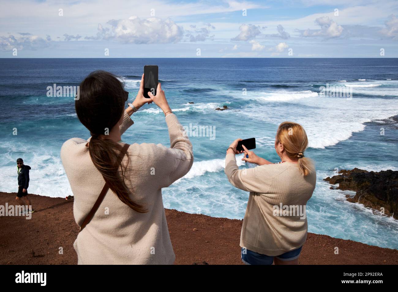 Weibliche Touristen fotografieren mit ihren Telefonen auf dem beliebten Aussichtspfad mirador el golfo Küstenaussichtspfad Lanzarote, Kanarische Inseln, Spanien Stockfoto