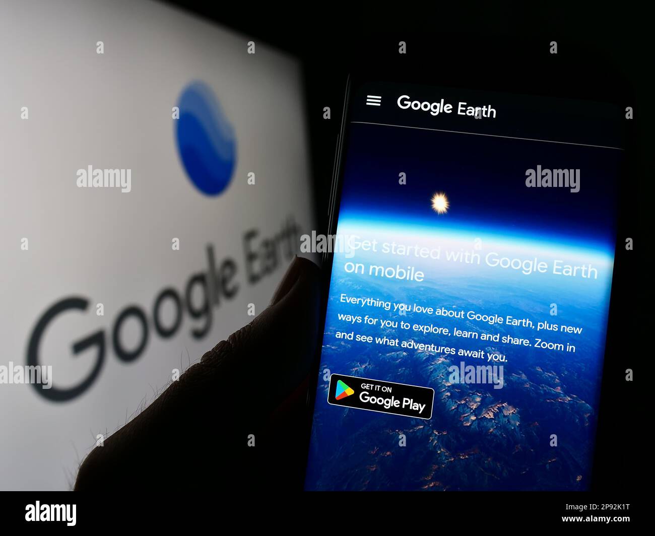 Person, die ein Mobiltelefon mit einer Webseite der Satellitenbildsoftware Google Earth auf dem Bildschirm vor dem Logo hält. Konzentrieren Sie sich auf die Mitte des Telefondisplays. Stockfoto