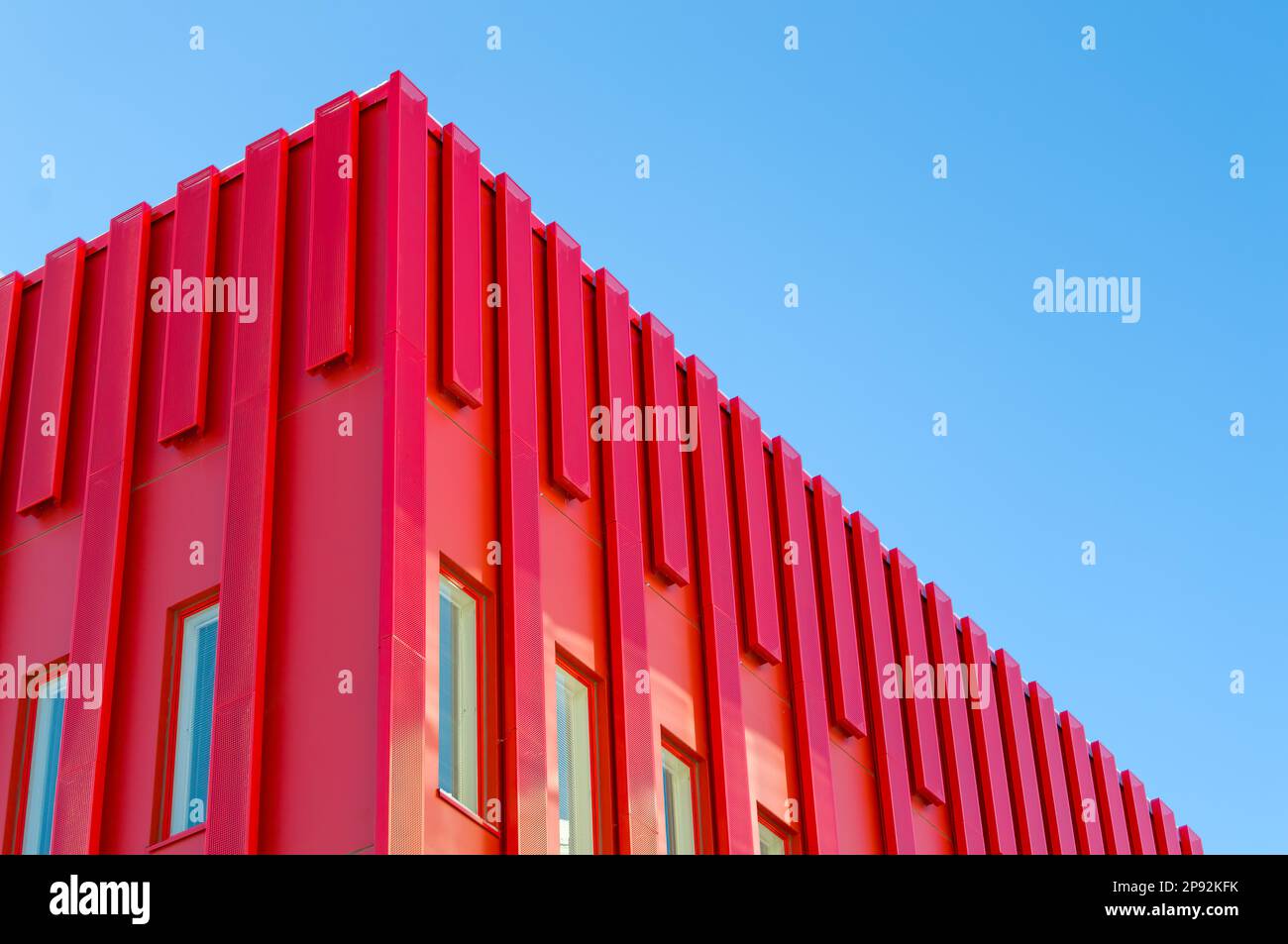 Modernes rotes Bürogebäude. Metallbleche, die die Außenseite der Struktur abdecken. Einzigartiges futuristisches Gebäude. Klarer Himmel hinten Stockfoto