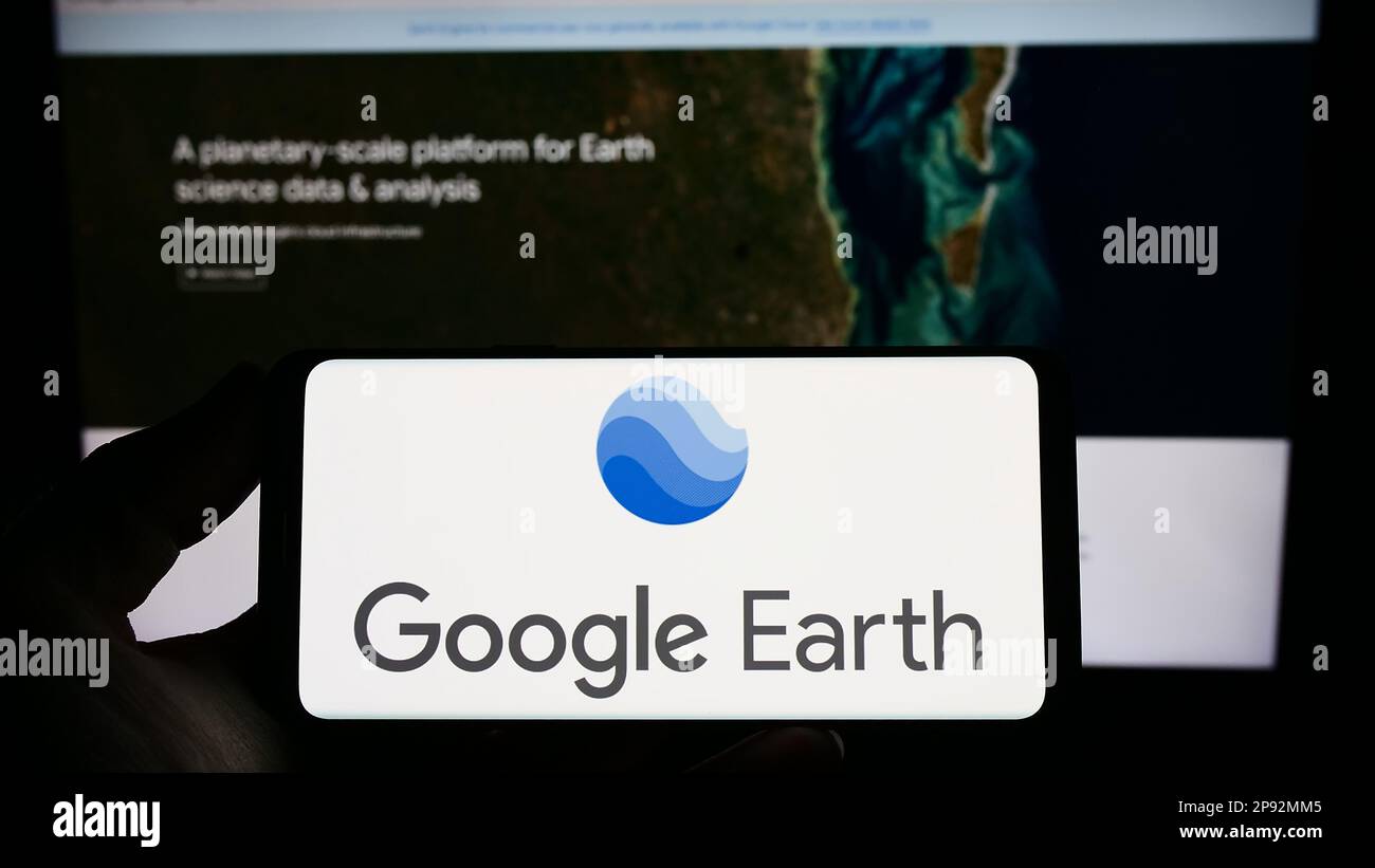 Person, die ein Smartphone mit dem Logo der Satellitenbildsoftware Google Earth auf dem Bildschirm vor der Website hält. Konzentrieren Sie sich auf das Display des Telefons. Stockfoto
