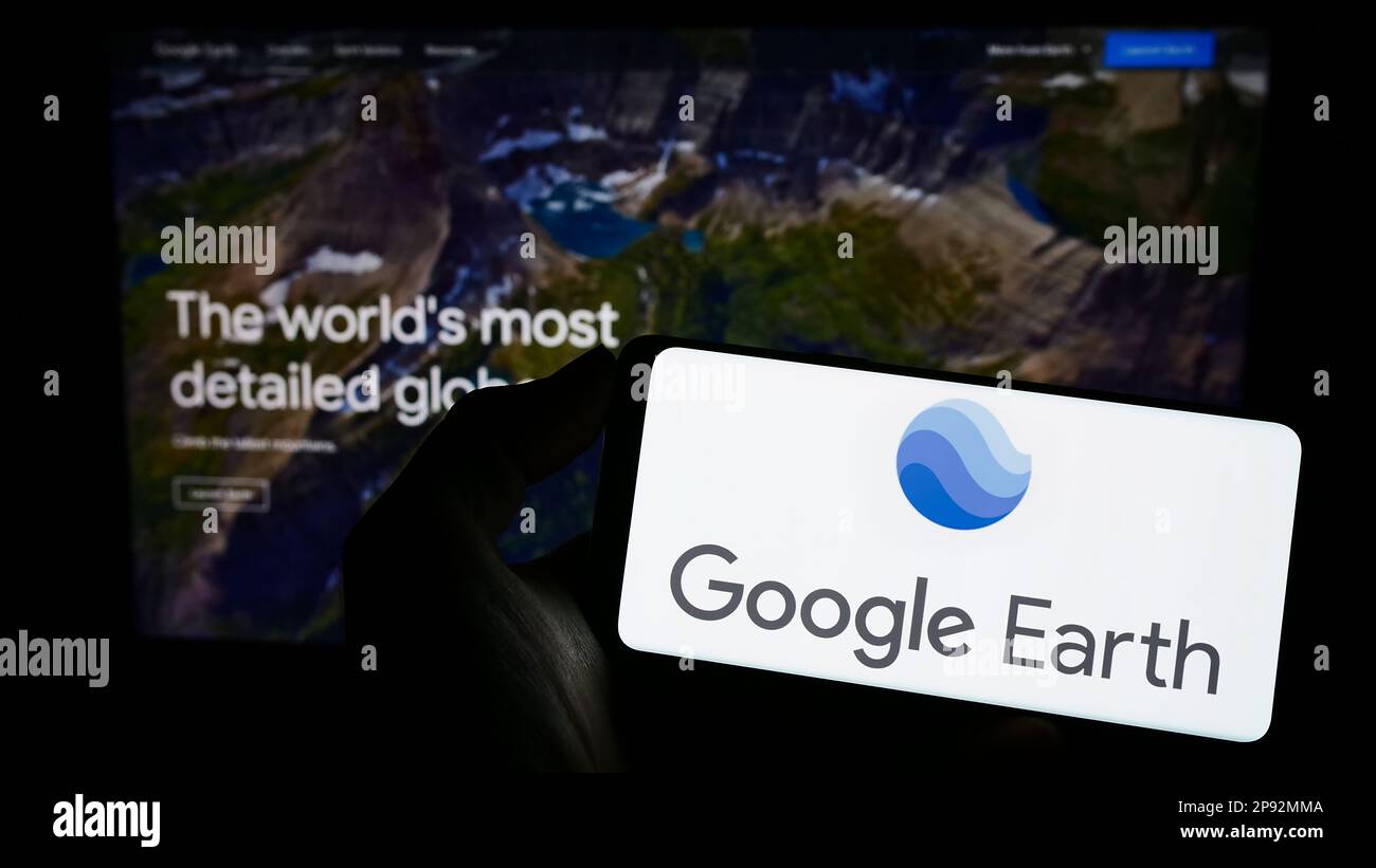 Person, die ein Mobiltelefon mit dem Logo der Satellitenbildsoftware Google Earth auf dem Bildschirm vor der Webseite hält. Konzentrieren Sie sich auf das Display des Telefons. Stockfoto