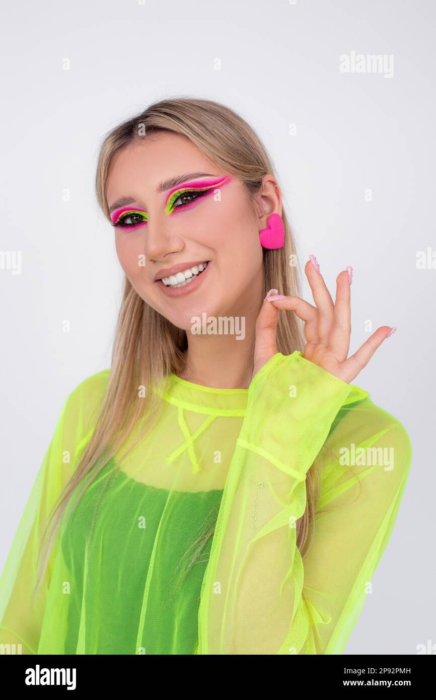 Es ist alles gut. Eine junge Blondine mit leuchtendem Neon-Make-up lächelt und zeigt mit ihren Fingern, dass alles in der Kamera gut läuft. Stockfoto