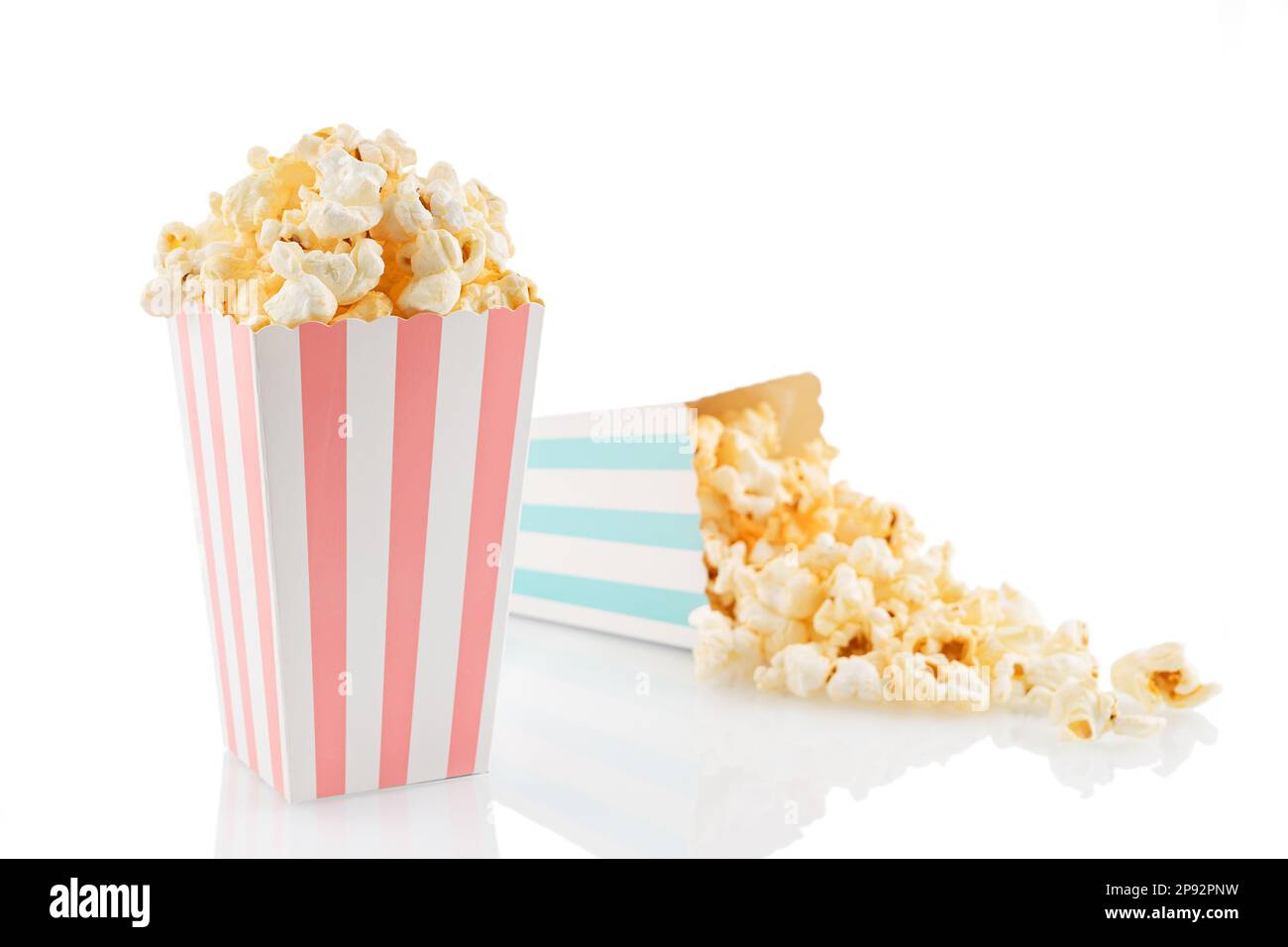 Zwei pinkfarbene und blau-weiß gestreifte Eimer mit leckerem Käsepopcorn, isoliert auf weißem Hintergrund. Schachtel mit Streuung von Popcornkörnern. Filme, Stockfoto