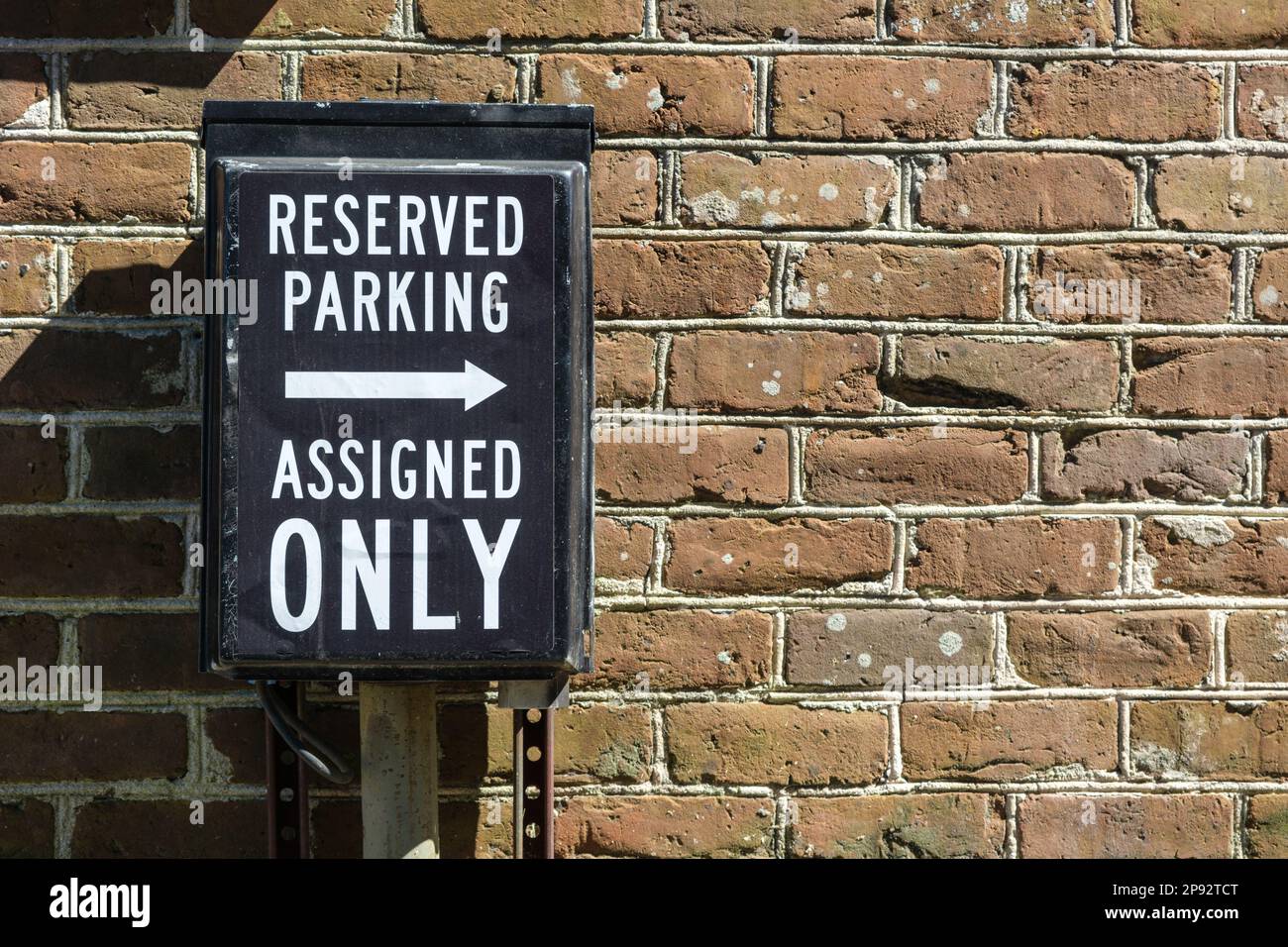 Reservierter Parkplatz und Schild nur für zugewiesene Parkplätze vor einer roten Backsteinmauer Stockfoto