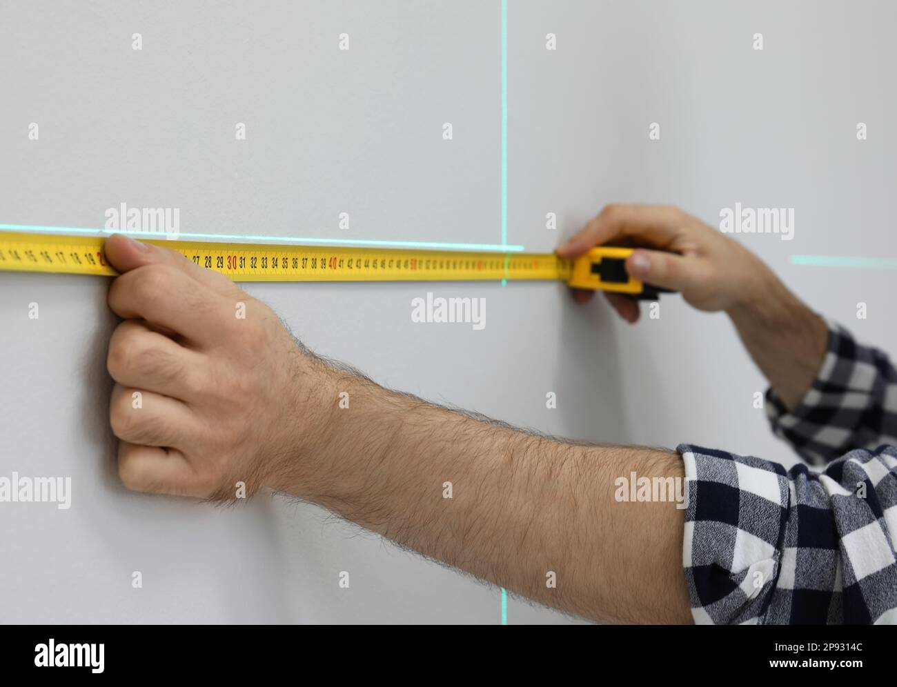 Mann, der eine Kreuzlinien-Laserwaage und Klebeband für genaue Messungen an einer leichten Wand verwendet, Nahaufnahme Stockfoto