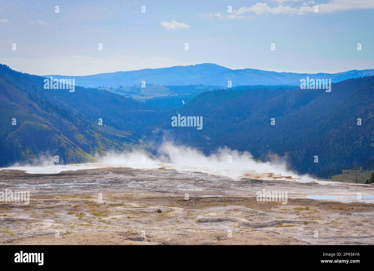 Im Yellowstone-Nationalpark erhebt sich Dampf aus einer heißen Quelle vor einer blauen Berglandschaft Stockfoto