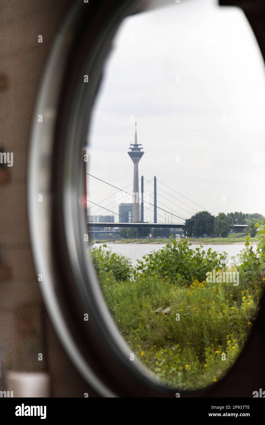 Blick durch ein Bullauge eines Rheinschiffs zum Düsseldorfer Fernsehturm und zur Rheinbrücke Stockfoto