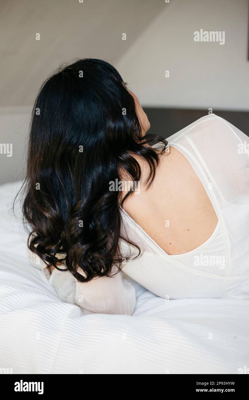 Rückansicht einer Frau mit langen schwarzen Haaren, die auf dem Bett ruht Stockfoto