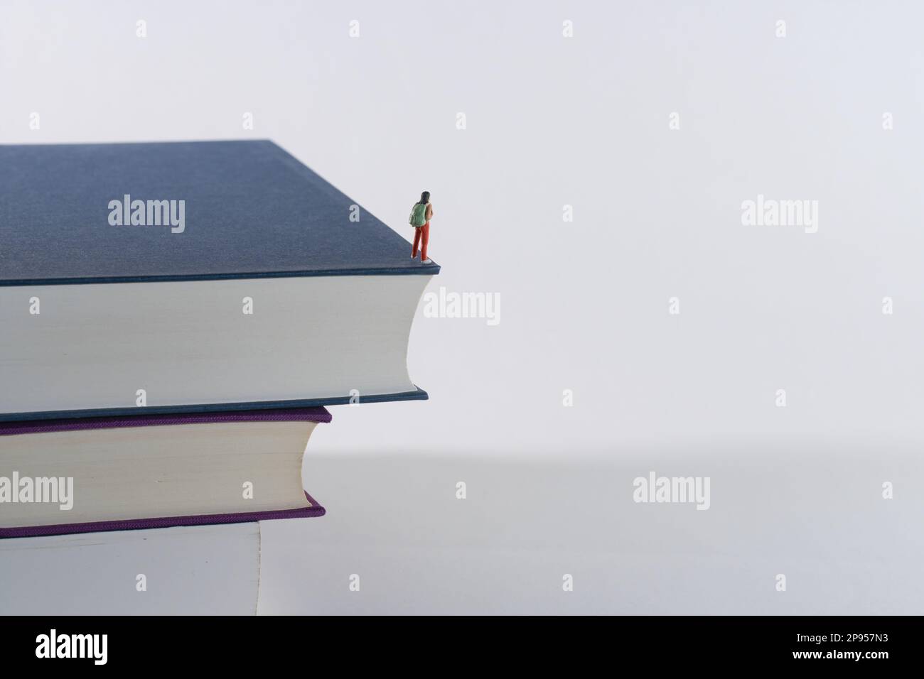 Mann mit Rucksack, Tourist, Anhalter schaut aus einem großen Stapel Bücher, weißer Hintergrund Stockfoto