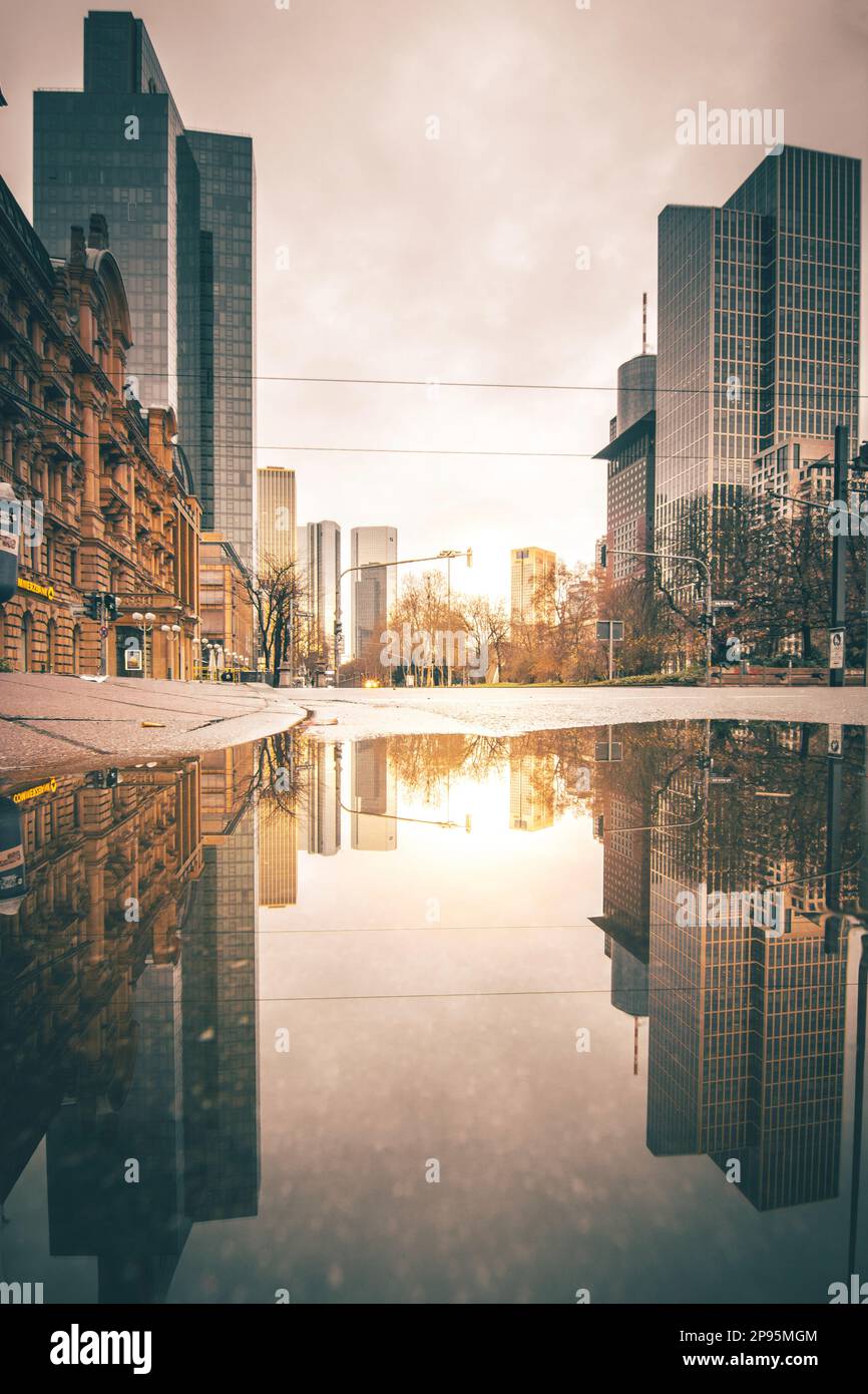 Reflexionen in Frankfurt am Main. Die Stadt, Straßen und Wolkenkratzer spiegeln sich nach Regen in den Pfützen der Straßen wider. Bankenviertel und Wolkenkratzer am Morgen Stockfoto