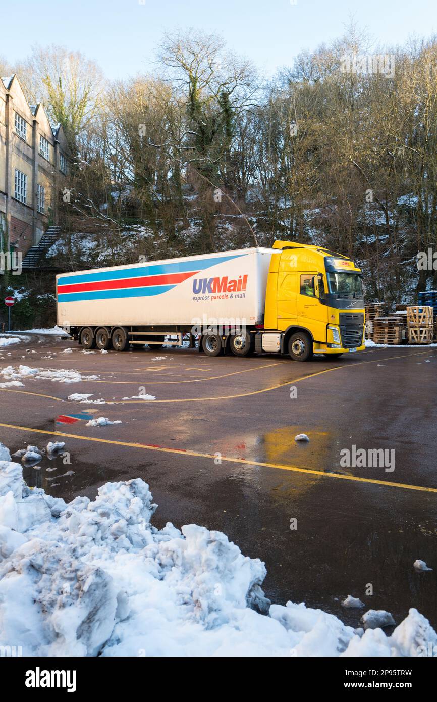 DHL-lkw in gelber Aufmachung mit UKmail-Anhänger, der vor einer Steinfabrik geparkt ist und Schnee auf dem Boden hat. Stockfoto