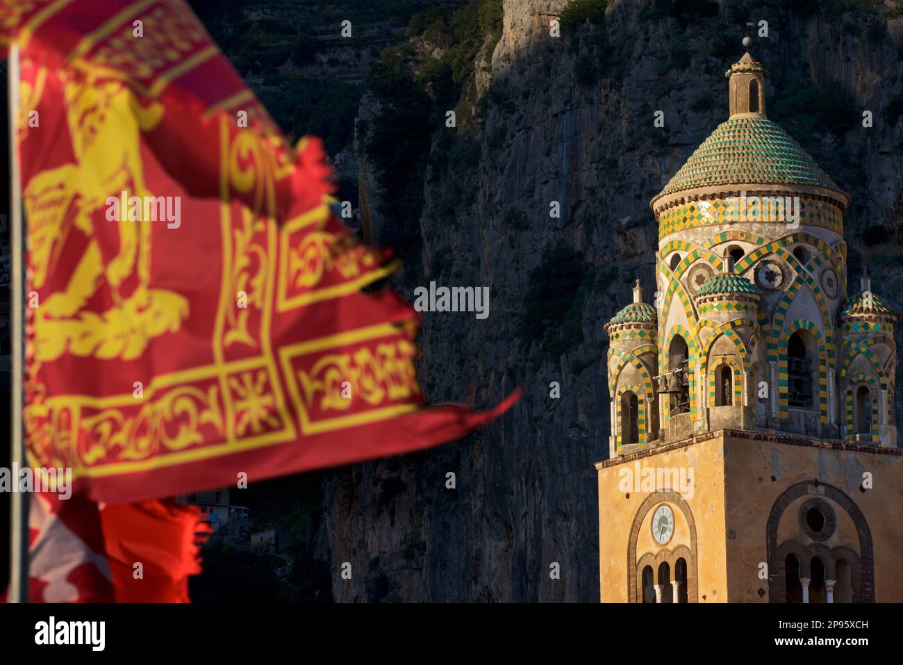 Glockenturm des Duomo di Sant Andrea (St. Andrew's Cathedral). Amalfi, Salerno, Italien Amalfiküste. Die Kathedrale, die im 9. Und 10. Jahrhundert begann, wurde mehrmals ergänzt und umgestaltet und überlagert arabisch-normannische, gotische, Renaissance- und Barockelemente, Und schließlich eine neue normannisch-arabisch-byzantinische Fassade aus dem 19. Jahrhundert. Die venezianische Flagge bläst im Wind Stockfoto