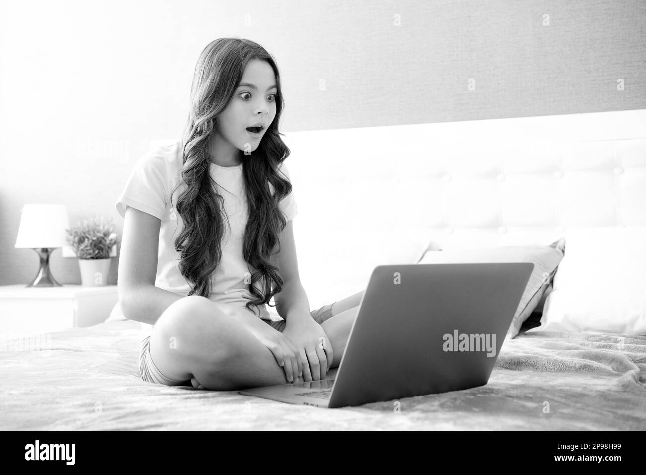 Teenager, Kind, das an einem Laptop-PC arbeitet, liegt im Bett und ruht sich zu Hause im Schlafzimmer aus. Teenager-Mädchen. Überraschtes Gesicht, überraschende Emotionen Stockfoto