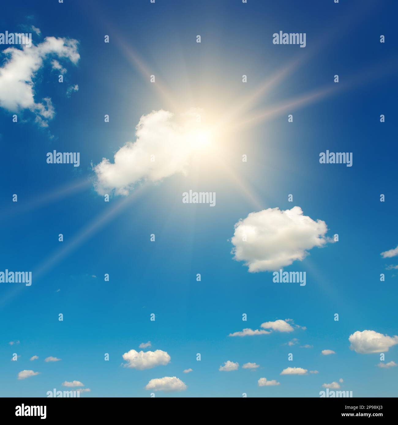 Blauer Himmel mit flauschigen Wolken und helle Sonne mit Strahlen. Stockfoto