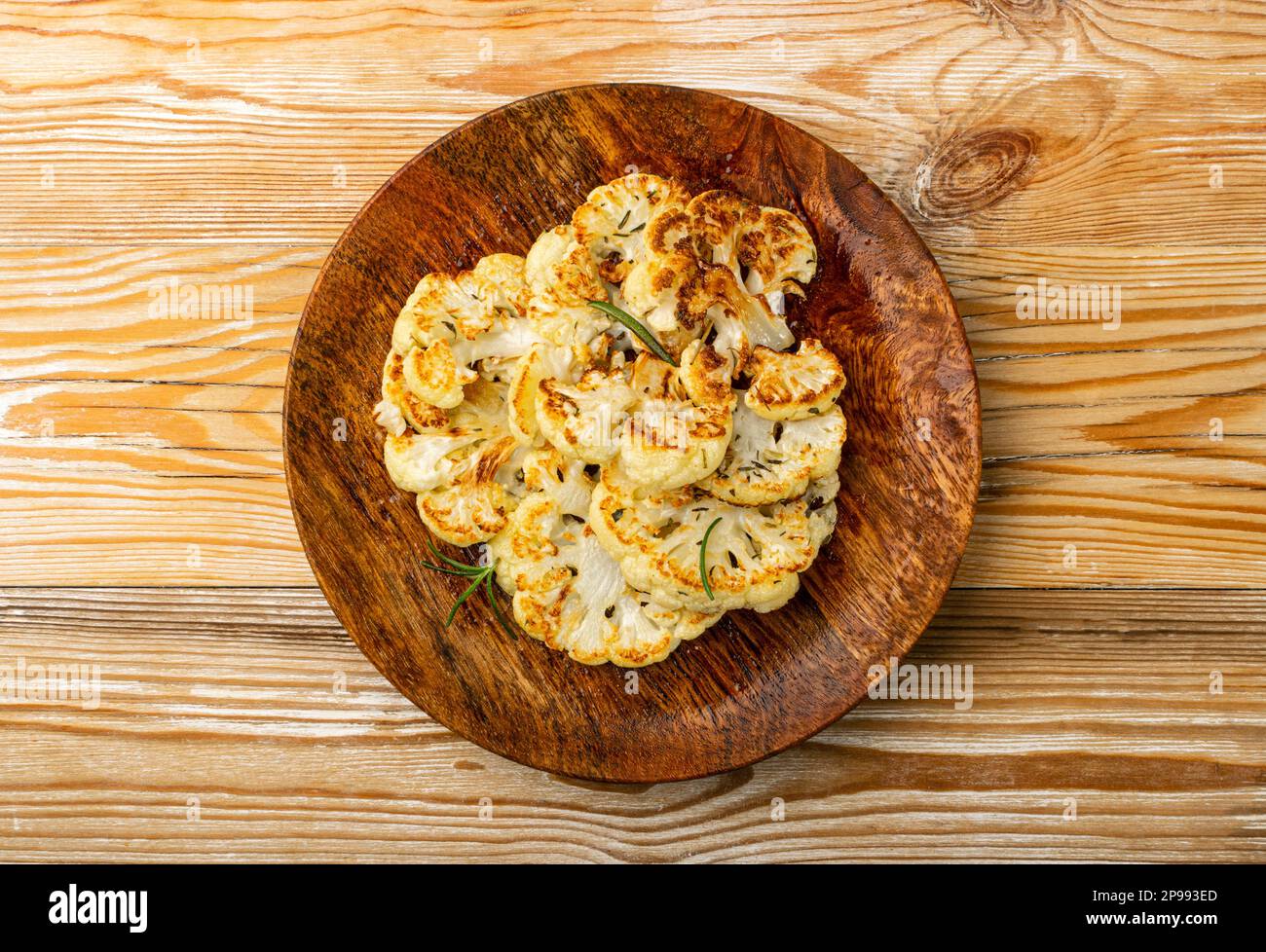 Gebratene Blumenkohlscheiben auf Holzteller, gebackene Blumenkohlsteaks, gebratenes Kohlsteak mit Kräutern, Draufsicht Stockfoto