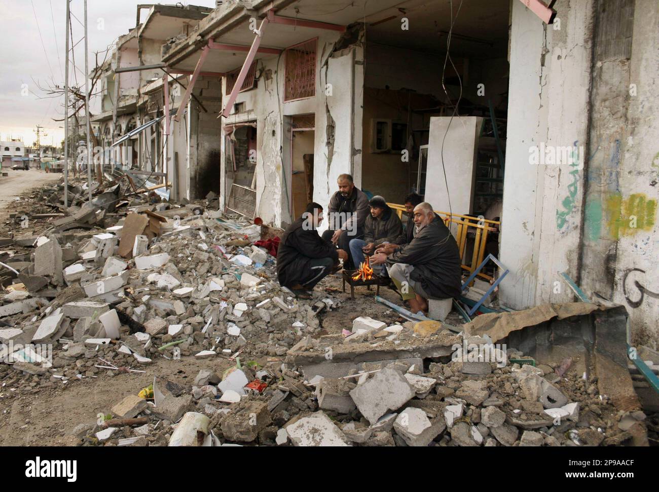 Palestinians sit beside a fire in the rubble of a destroyed house that ...