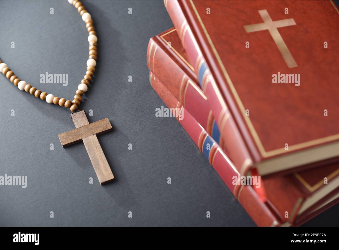 Ein Haufen religiöser Bücher und ein Kreuz mit Holzperlen auf einem schwarzen Tisch. Erhöhte Ansicht von oben. Stockfoto