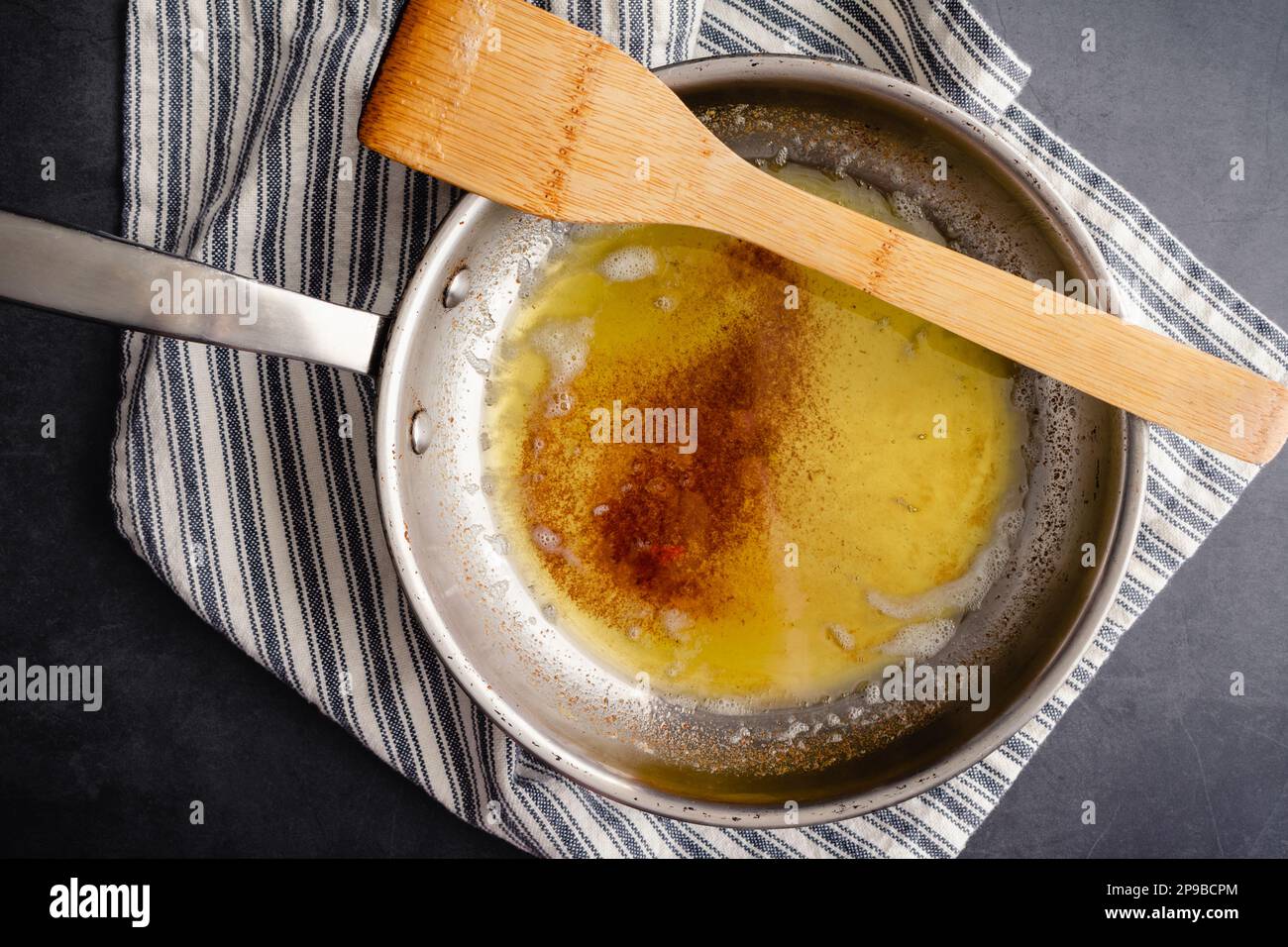 Braune Butter in einer Pfanne aus Edelstahl mit einem Holzspatel: Blick von oben auf braune Butter in einer Pfanne auf einem Küchentuch Stockfoto