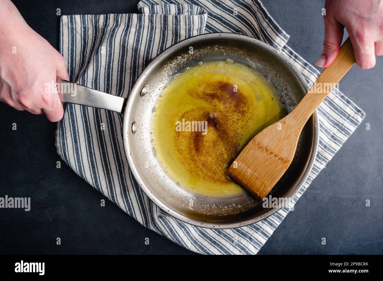 Braune Butter in einer Pfanne aus Edelstahl mit einem Holzspatel: Von oben betrachtet, wie braune Butter in einer Bratpfanne gerührt wird Stockfoto