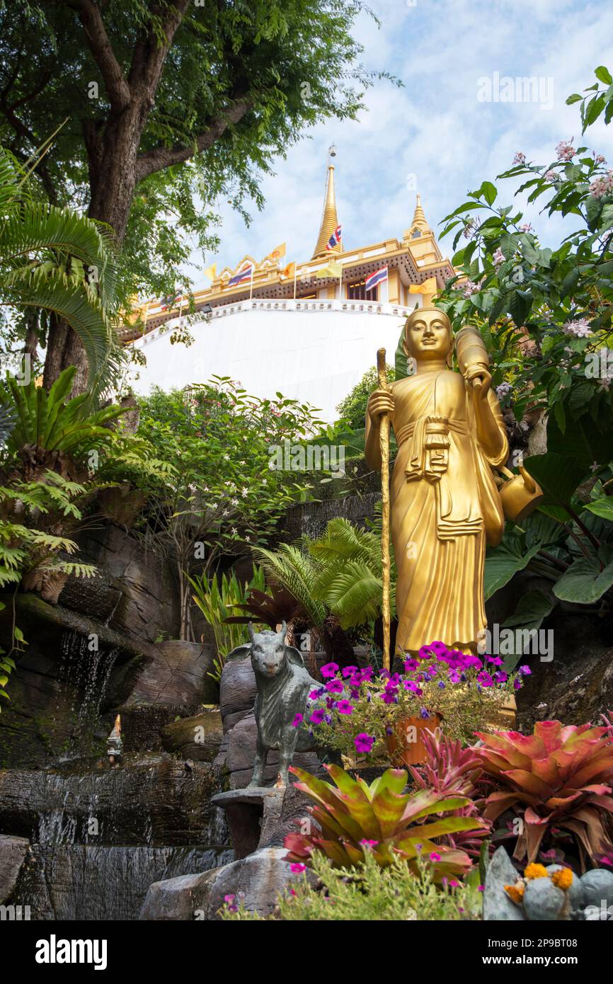 Goldene Buddha-Statue im tropischen Garten mit Wasserfall im Wat Saket goldenen Berg Tempel in Bangkok Stockfoto