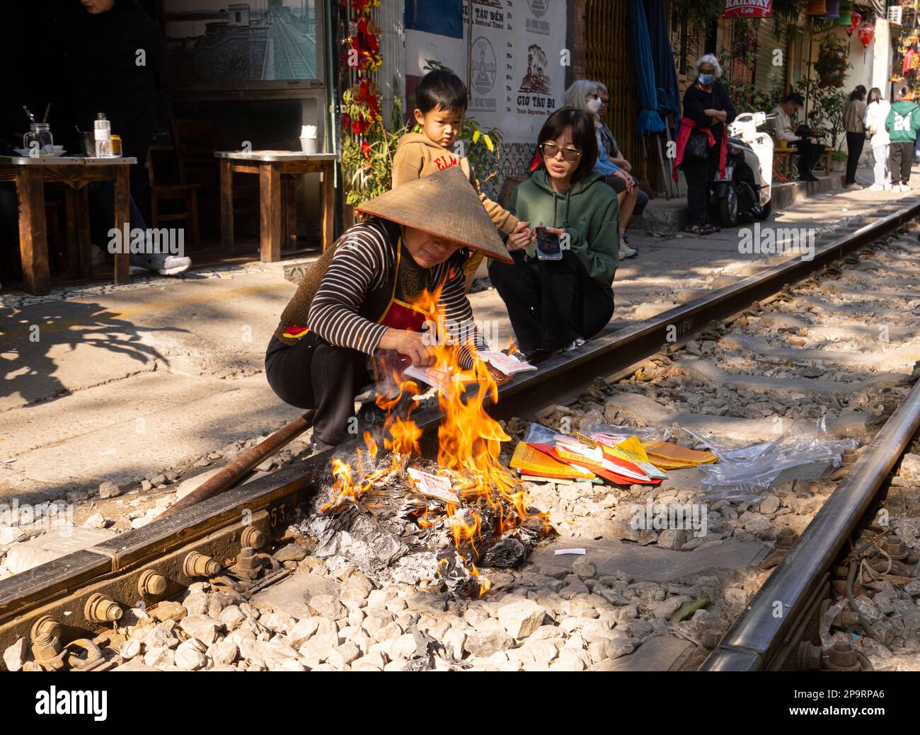 Hanoi, Vietnam. Jnauary 2023. Eine Frau verbrennt tiền âm phủ, Votivopfer für Vorfahren entlang der Gleise vor ihrem Haus im alten Quart Stockfoto