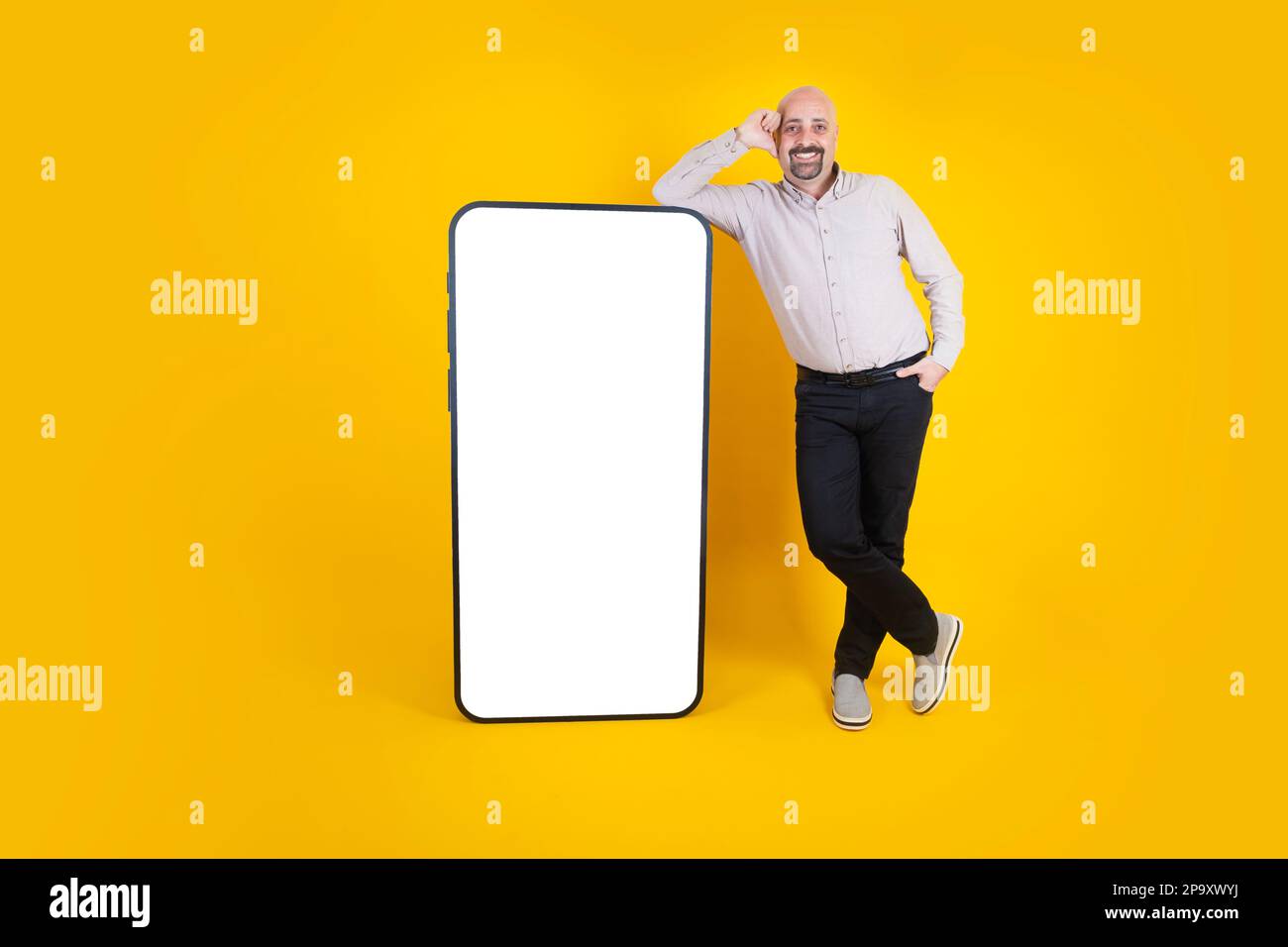 Dasual gekleideter, durchgehender, fröhlicher Mann mit großem Handy. Weißes Mobiltelefon-Modell mit leerem Bildschirm. Smartphone-Anwendung, Website. Stockfoto
