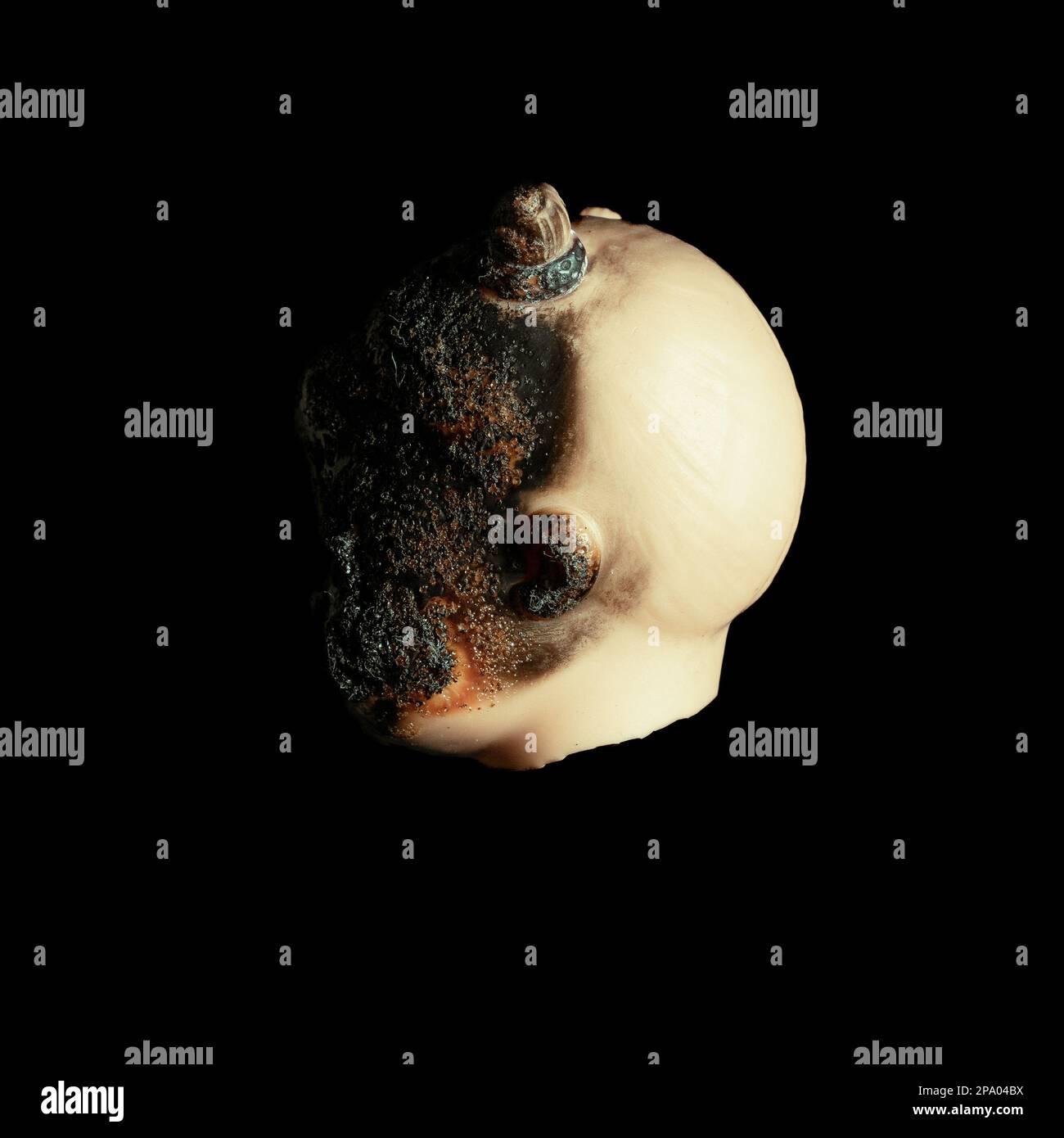 Unheimlich isoliert gespenstisch besessenes Baby Mädchen Puppenkopf gruselig verbranntes Gesicht mit grauem Auge auf schwarzem Hintergrund Nahaufnahme Makro Stockfoto