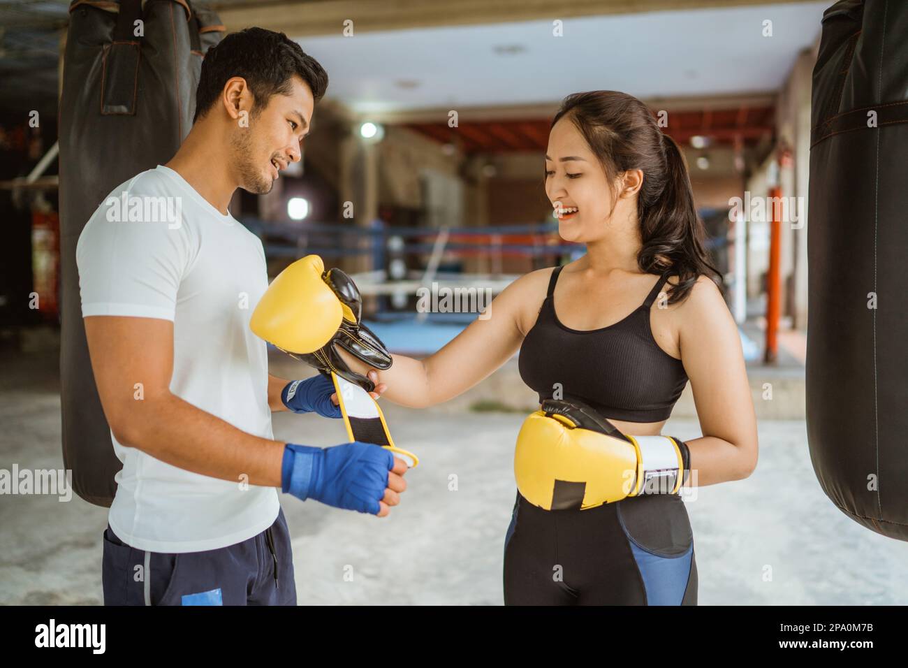 Ein Boxtrainer, der der Boxerin hilft, die Boxhandschuhe zu tragen Stockfoto