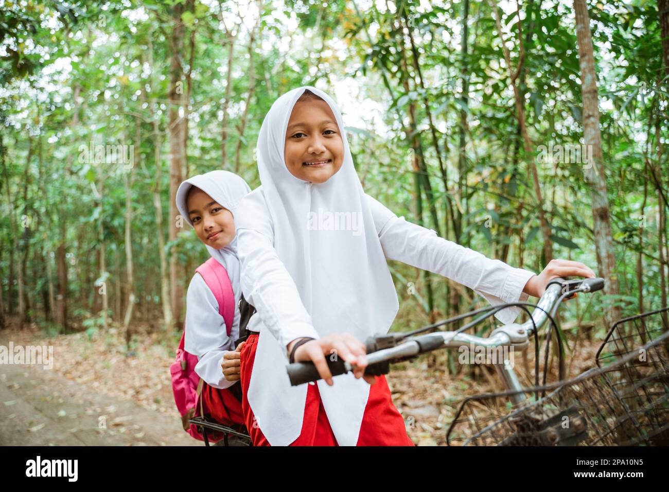Zwei hübsche Mädchen in Grundschuluniform, die zusammen Fahrrad fahren Stockfoto