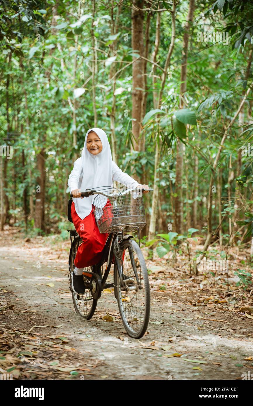 Eine schöne Grundschülerin in Uniform, die mit dem Fahrrad durchs Land fährt Stockfoto