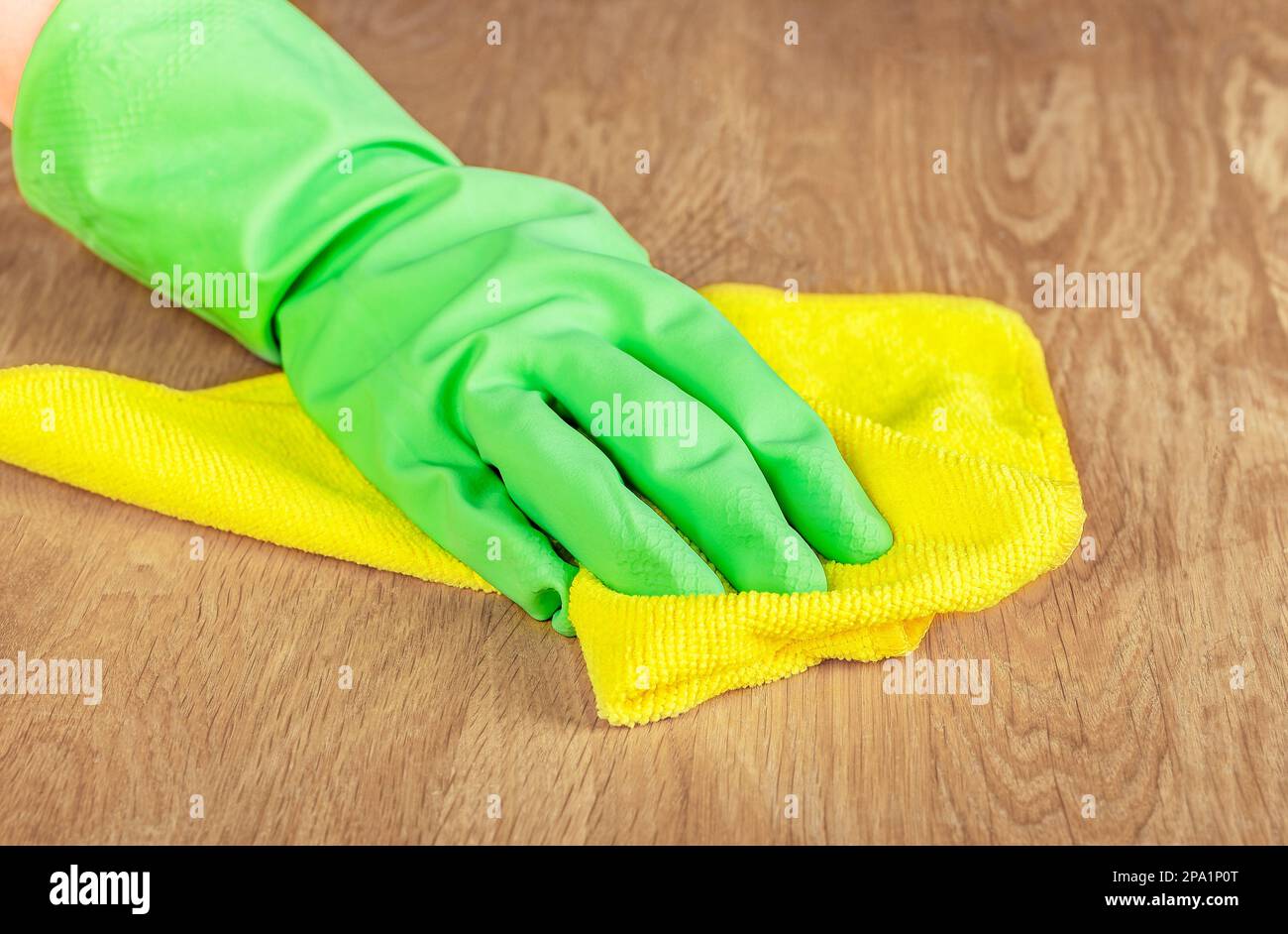Grüner Handschuh zum Abwischen von Staub vom Holzschreibtisch mit Mikrofasertuch und Wischtuch. Stockfoto