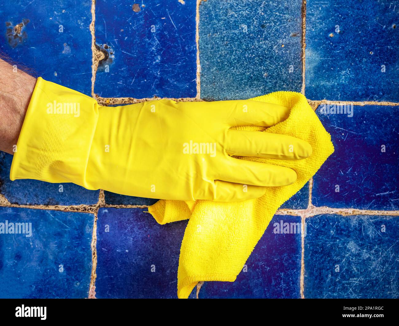 Gelber Handschuh zum Reinigen alter schmutziger Fliesen im Badezimmer, Polieren mit Mikrofasertuch. Stockfoto