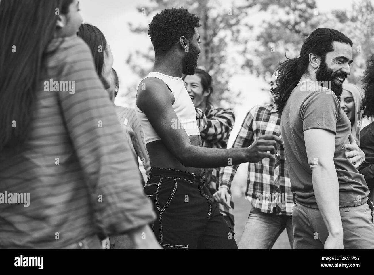 Junge, vielfältige Menschen, die gemeinsam im Freien tanzen - Schwerpunkt auf afrikanischem Schwulenkopf - Schwarz-Weiß-Schnitt Stockfoto
