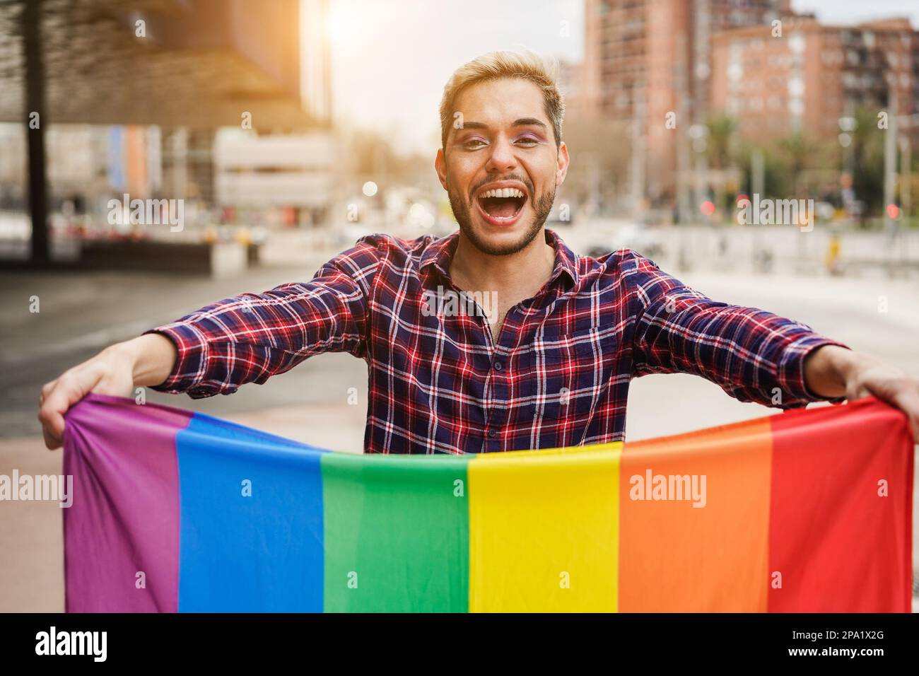 Fröhlicher schwuler Mann mit Make-up und lgbt-Regenbogenflagge im Freien – Fokus auf das Gesicht Stockfoto