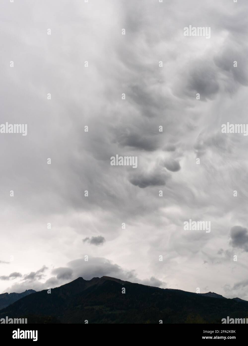 Abstrakter, ungewöhnlicher wolkiger Himmelshintergrund in milchig-grau und weiß und eine dunkle Silhouette in den Bergen Stockfoto