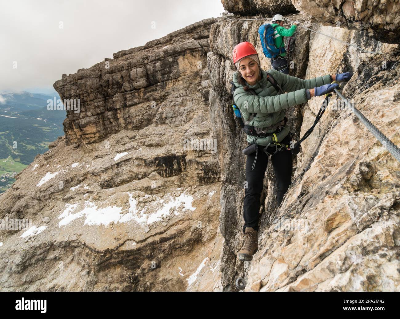 Gruppe junger Bergsteiger auf einer steilen Via Ferrata mit einem grandiosen Blick auf die italienischen Dolomiten in Alta Badia dahinter Stockfoto