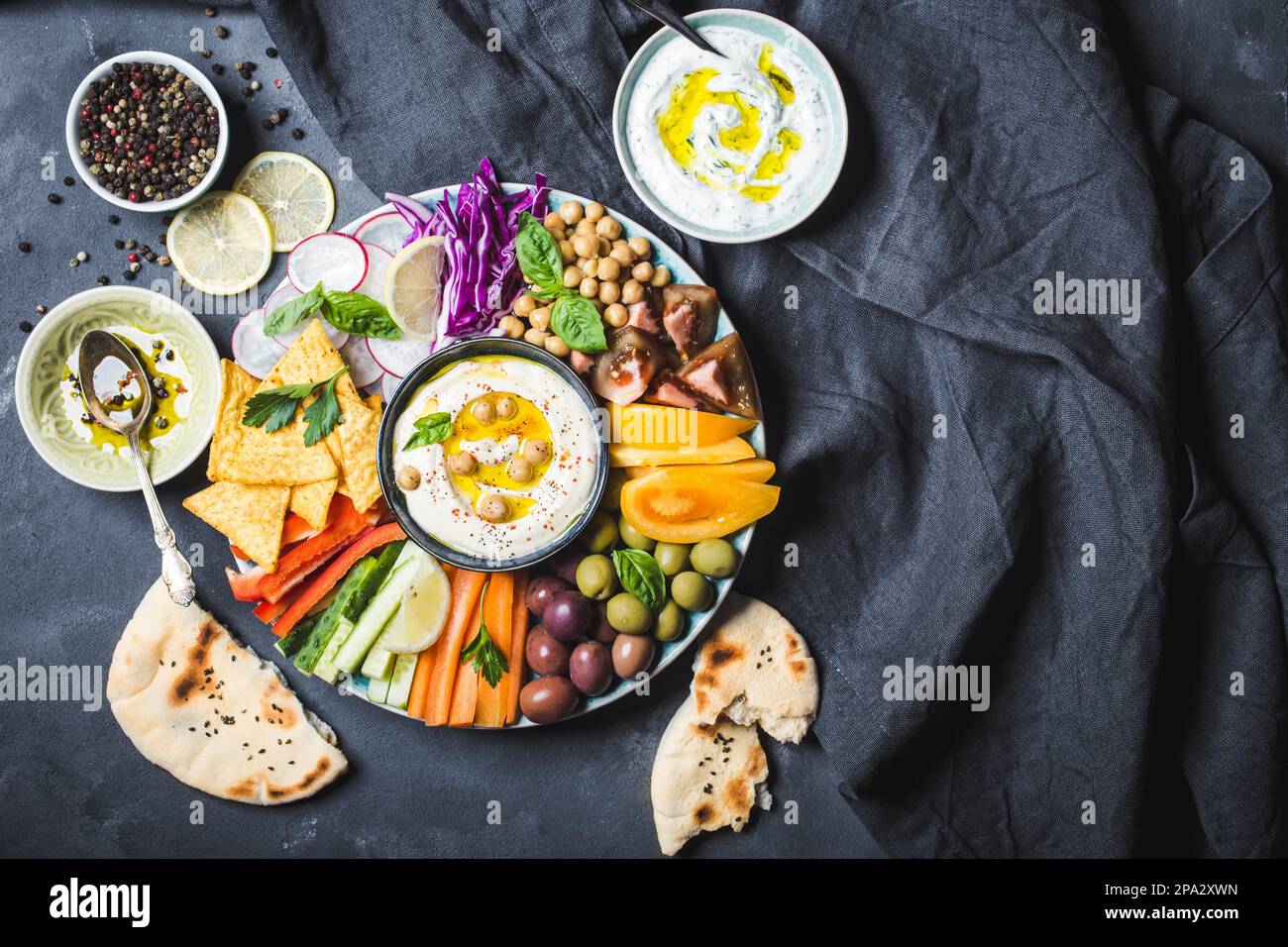 Meze-Platte mit Hummus, Joghurtdip und verschiedenen Snacks. Platz für Text. Hummus, Gemüsestangen, Kichererbsen, Oliven, Pita, Chips. Platte, Mitte Stockfoto