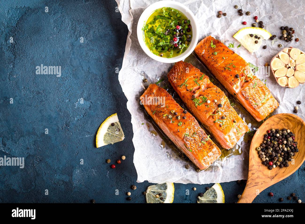 Köstliches gebratenes Lachsfilet, Gewürze auf blauem rustikalem Betonhintergrund. Gekochtes Lachssteak mit Pfeffer, Kräutern, Zitrone, Knoblauch, Olivenöl Stockfoto