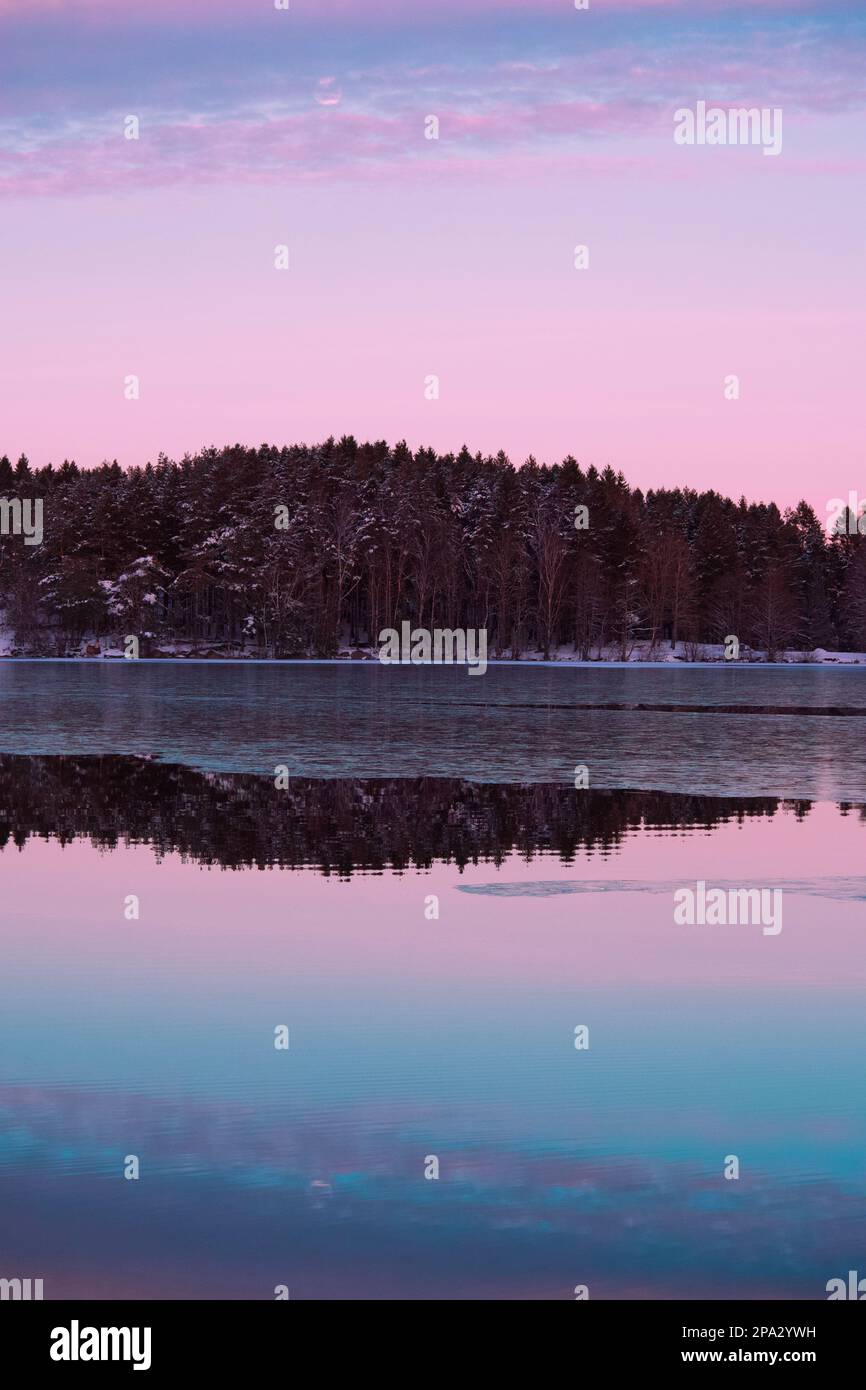 Sonnenuntergang über dem halbgefrorenen See mit einer Baumlinie am Horizont Stockfoto